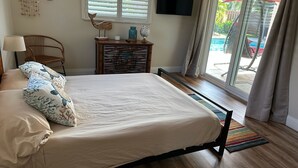 Un dormitorio con cama, sillón, cómoda, televisor y vistas al exterior.
