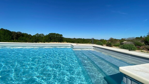 Une piscine d’un bleu éclatant, avec vue sur une colline boisée et un ciel dégagé.