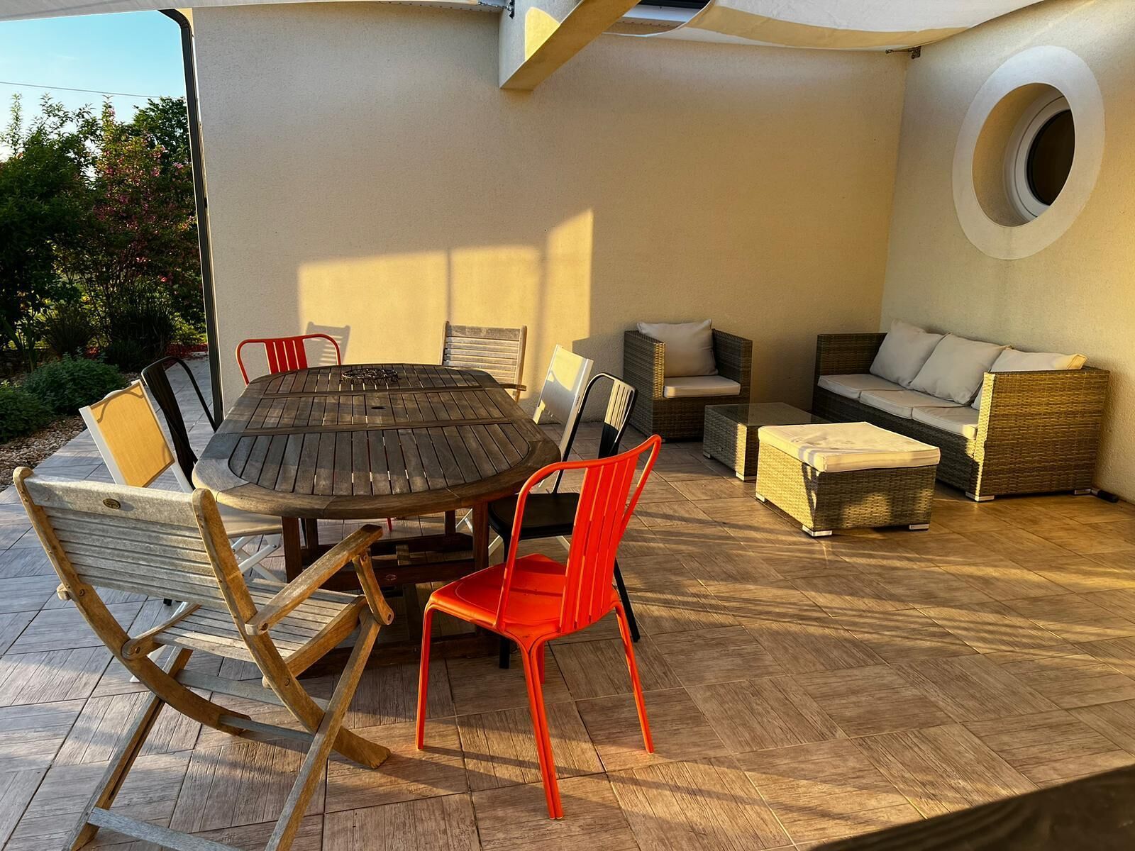 Een terras met een ronde tafel, rieten meubels en een rond raam.