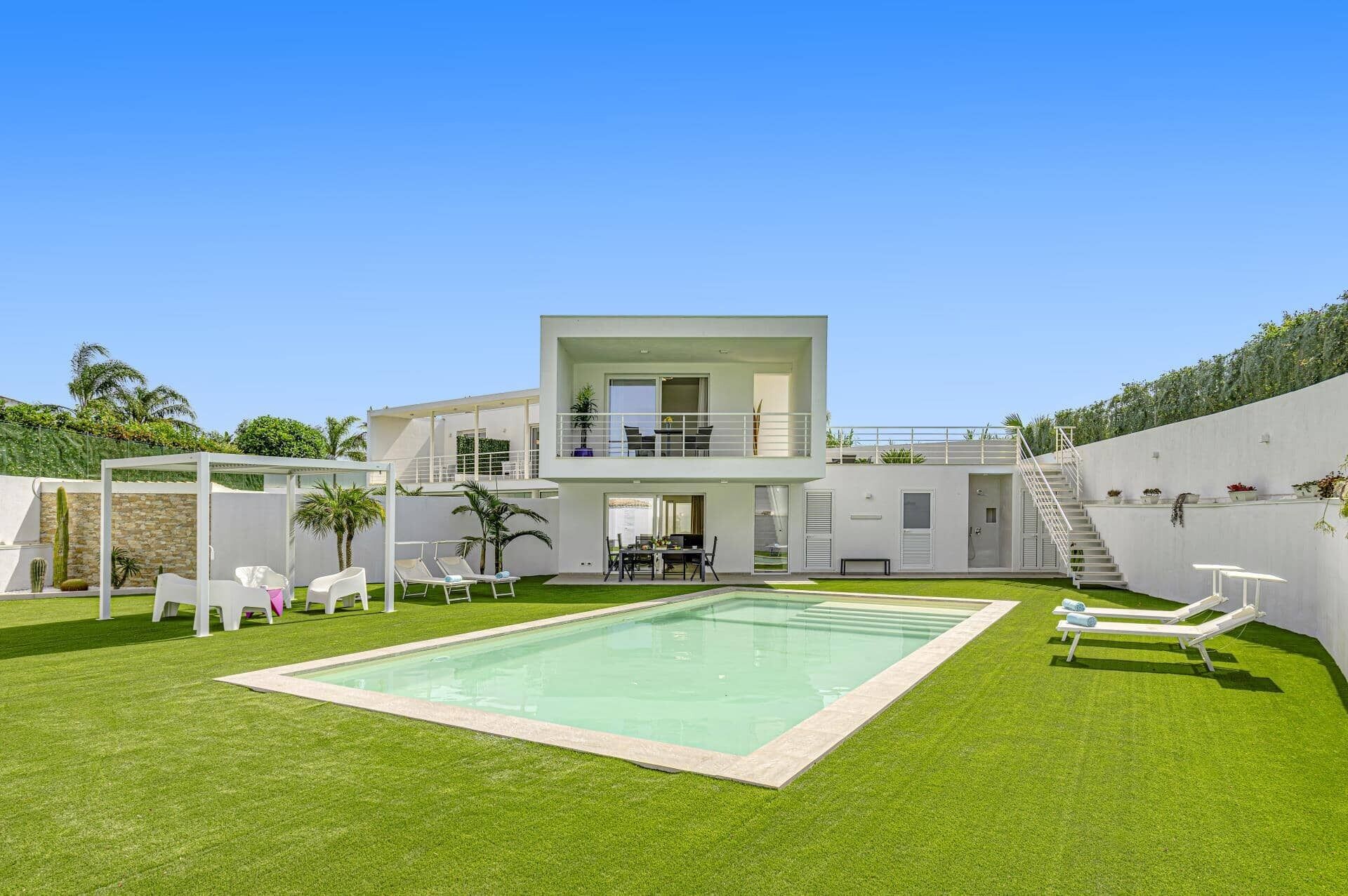 A modern two-story house with a swimming pool, outdoor seating, and a balcony.