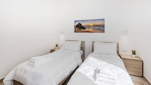 Habitación de hotel con dos camas individuales, ropa de cama blanca, un cuadro de una puesta de sol sobre el océano y lámparas de noche.