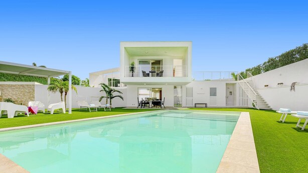 Una casa moderna de dos pisos con piscina, asientos exteriores y una escalera que conduce a un balcón.