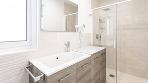 Een moderne badkamer met een wastafel met twee kommen, een grote spiegel, een haardroger en een douchecabine met glazen wanden.