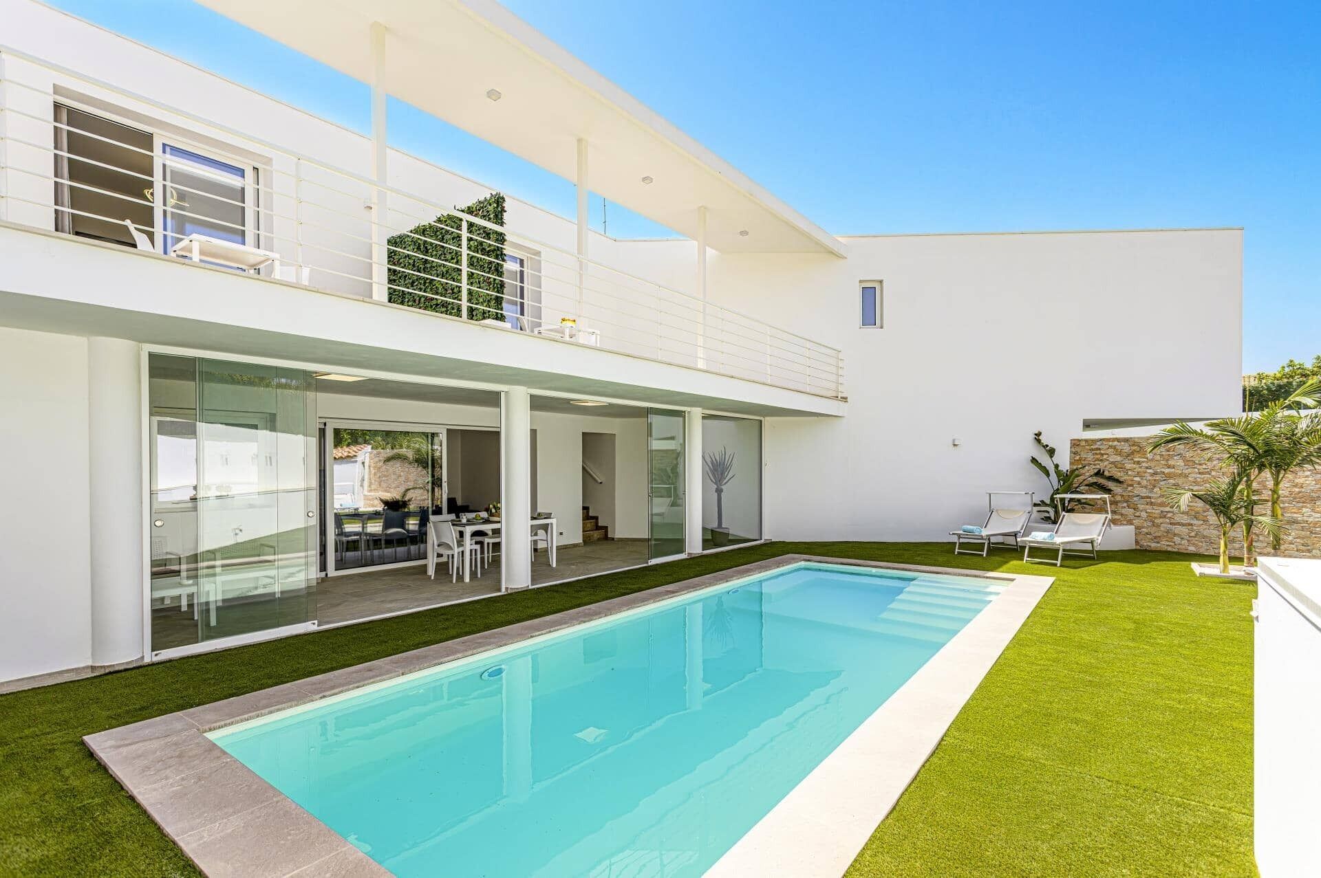 Una casa moderna de dos pisos con piscina, un patio cubierto y un muro de piedra.