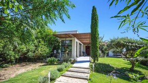 Una casa moderna con un porche cubierto, un sendero de piedra que lleva a la entrada y abundante vegetación alrededor de la propiedad.