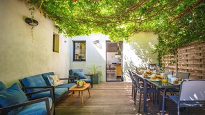 Un patio acogedor con terraza de madera, asientos con cojines azules y una mesa de desayuno servida con comida y bebidas.