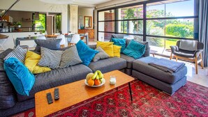 Una sala de estar moderna con un sofá seccional gris, almohadones coloridos, una mesa de centro de madera con fruta y un vaso de leche, y una alfombra roja estampada.