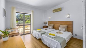 A hotel room with two beds, a wooden floor, a balcony with a view, and a ceiling fan. - Villa Casa Jasmim by Villa Plus (Quarteira)