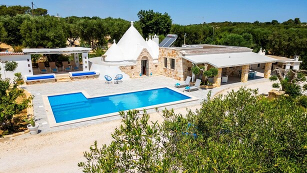 A poolside area with a clear blue pool, lounge chairs, and a stone building with a conical roof. - Villa Trullo Famigiu by Villa Plus (Grottaglie)