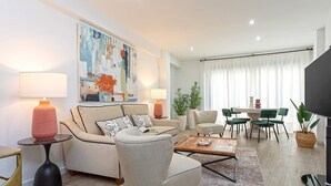 A modern living room with a sofa, armchairs, a coffee table, and a dining area with chairs and a table.