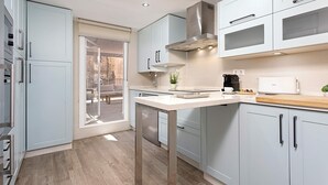 A modern kitchen with light blue cabinets, a stainless steel range hood, and a large window overlooking a balcony.