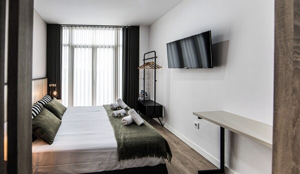 A modern hotel room with a bed, a TV mounted on the wall, and a bedside table. - San Juan Suites (Badajoz)
