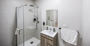 A modern bathroom with a glass-enclosed shower, a wooden vanity, and a white sink. - San Juan Suites (Badajoz)