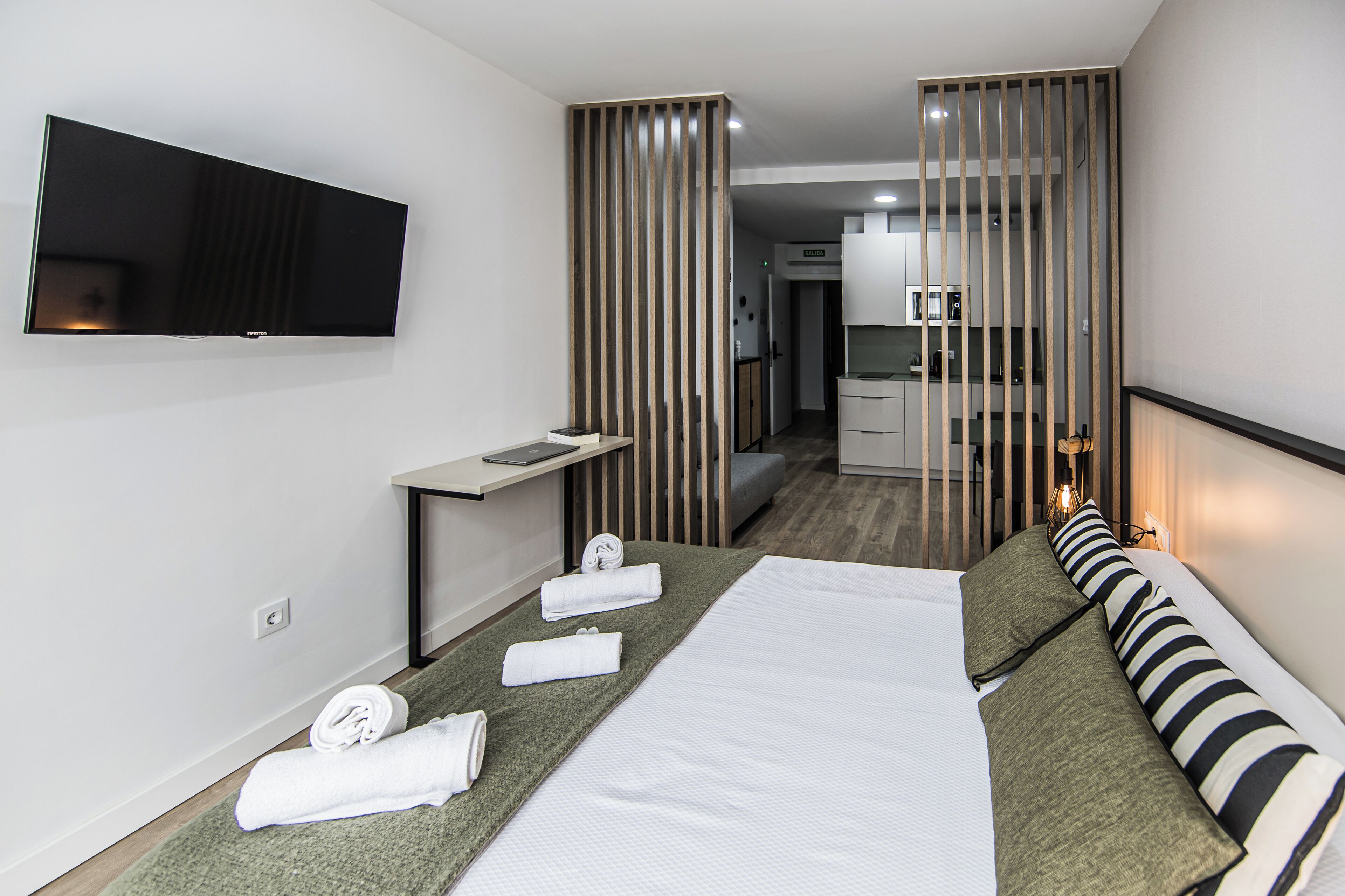 A hotel room with a bed, a desk, a flat-screen TV, and a kitchenette.