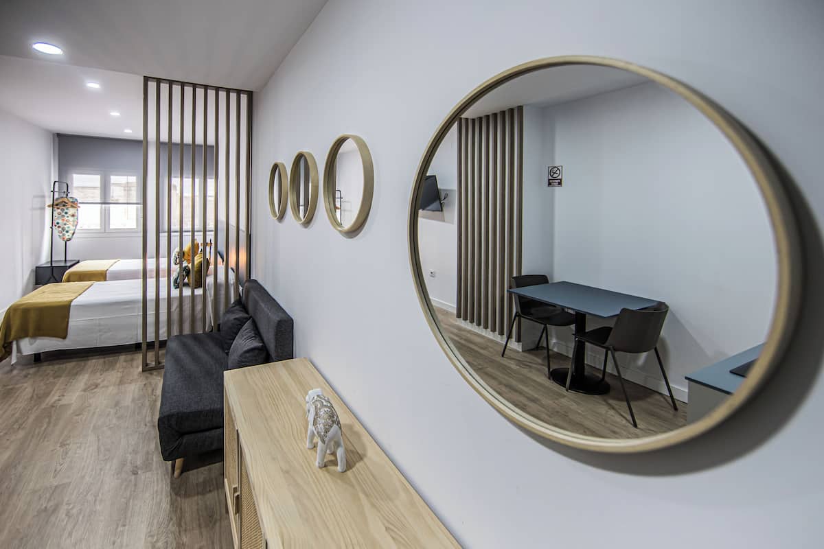 Une chambre d’hôtel moderne équipée d’un lit, d’un canapé, d’un bureau avec des chaises et d’un grand miroir.