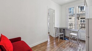 A small, bright room with a wooden floor, a red chair, a white table with two chairs, and a window overlooking a building. - ID 400- MEUNIERS near Bercy lively Area (Paris)