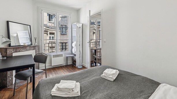 A compact bedroom with a bed, a desk, and a chair. There is a window with a view of buildings outside. - ID 400- MEUNIERS near Bercy lively Area (Paris)