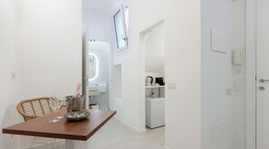 Uma sala de jantar minimalista com mesa de madeira, cadeiras de vime e uma tigela de vidro. Uma garrafa de champanhe está visível sobre a mesa.