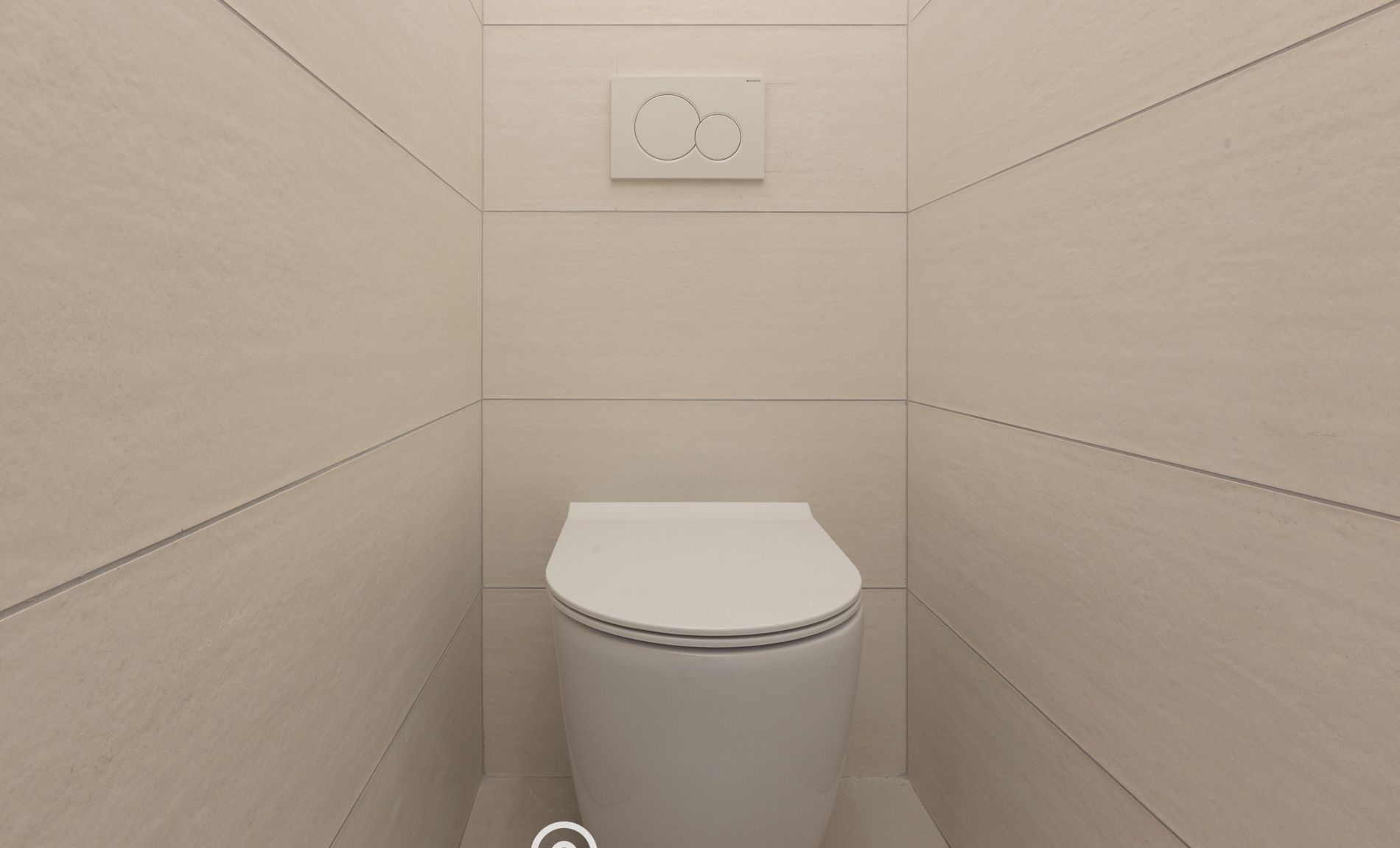 Une petite salle de bain moderne avec des toilettes blanches, un mécanisme de chasse d'eau mural et un sol carrelé.