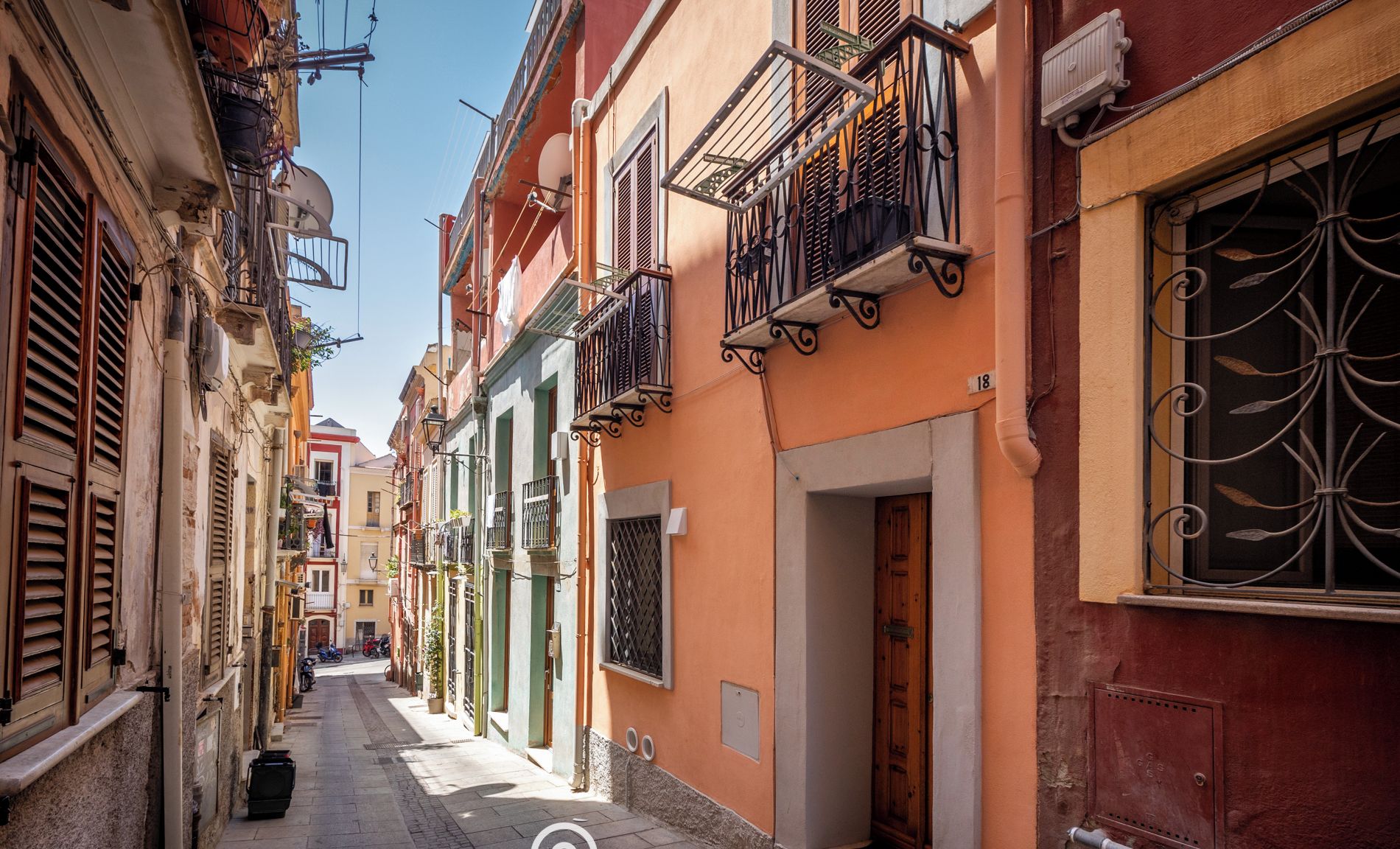 Una calle estrecha con edificios coloridos, una puerta visible y un letrero que dice Sardinia Hostay.