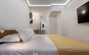 A modern hotel room with a bed, a bedside table, a mirror, and a TV mounted on the wall. - B Room - Studio Apartment, Sleeps 2 (Cagliari)