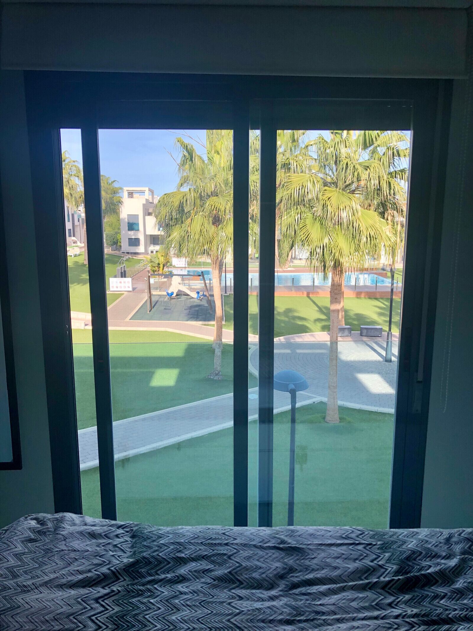 A room with a large window overlooking a well-maintained lawn, a pool, and a modern building.