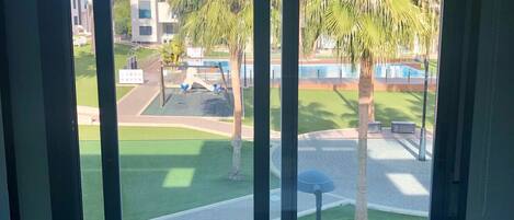 A room with a large window overlooking a well-maintained lawn, a pool, and a modern building.