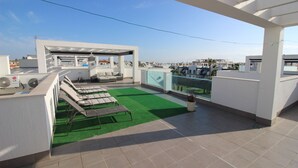 A rooftop terrace with a green artificial turf area, several lounge chairs, a small seating area, and a covered section with a fan and air conditioning unit. - Penthouse Oasis beach II La zenia (Orihuela Costa)