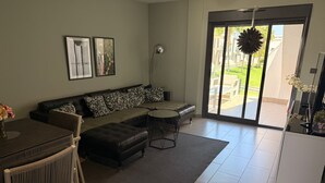 A living room with a sectional sofa, a dining table with chairs, a radiator, and a large window with a view of the outdoors. - Penthouse Oasis beach II La zenia (Orihuela Costa)