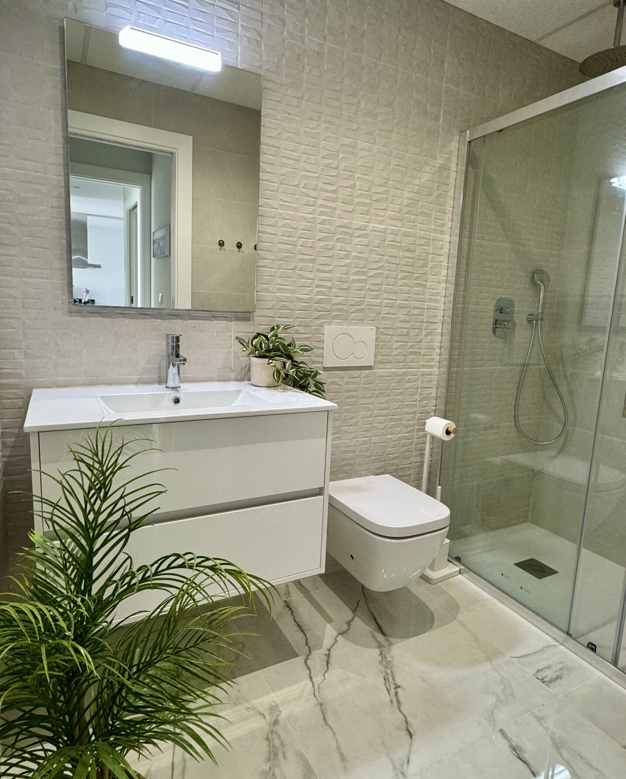 Un baño moderno con un tocador blanco, cabina de ducha de vidrio y una planta en maceta.