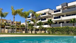 A modern hotel with a pool, palm trees, and a clear blue sky.
