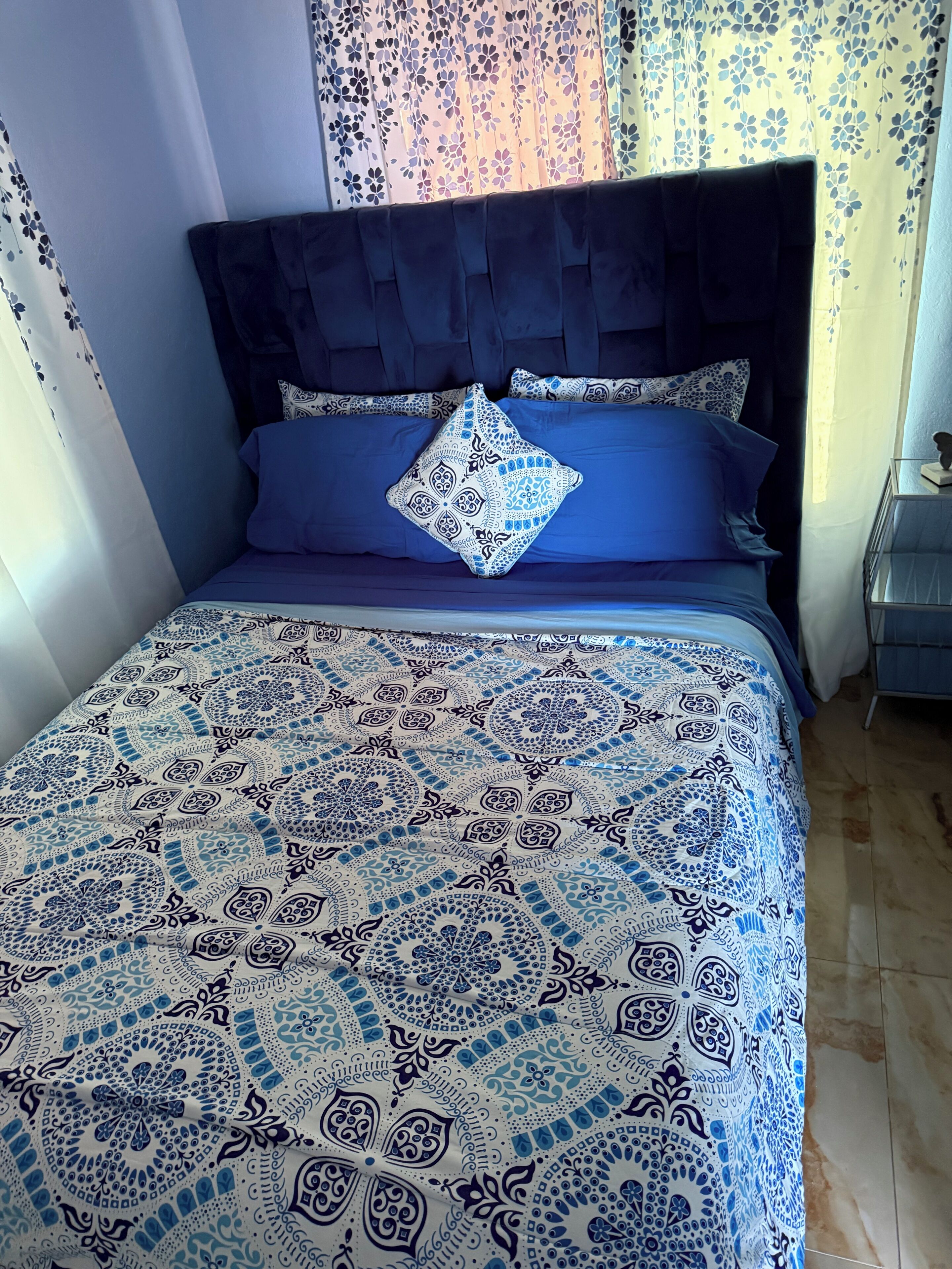 Un letto con una coperta a motivi, una testiera scura e un cuscino decorativo.