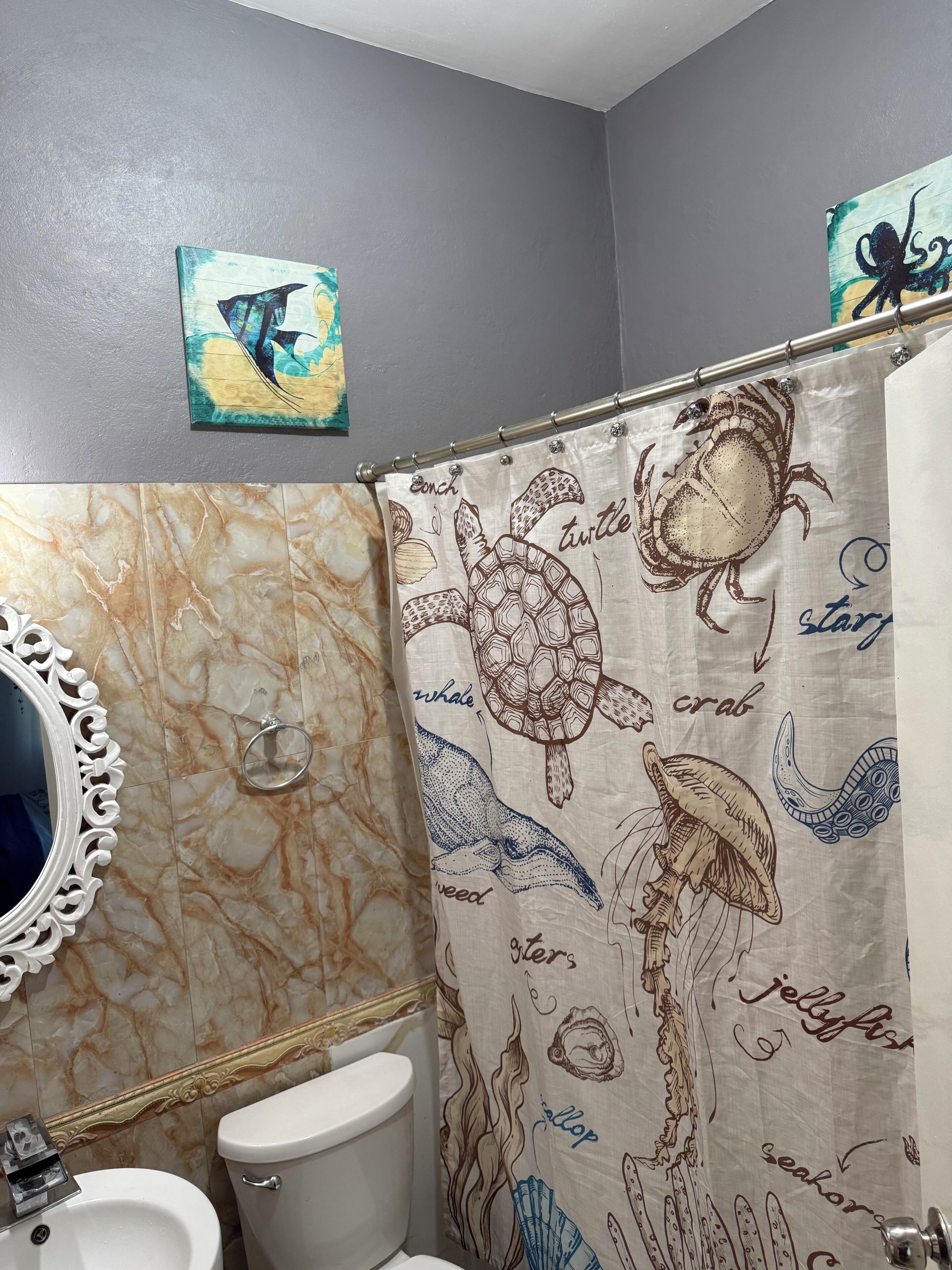 Une salle de bain avec un meuble-lavabo en marbre, des toilettes et un rideau de douche orné d’illustrations de la vie marine.