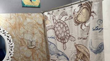 Une salle de bain avec un meuble-lavabo en marbre, des toilettes et un rideau de douche orné d’illustrations de la vie marine.