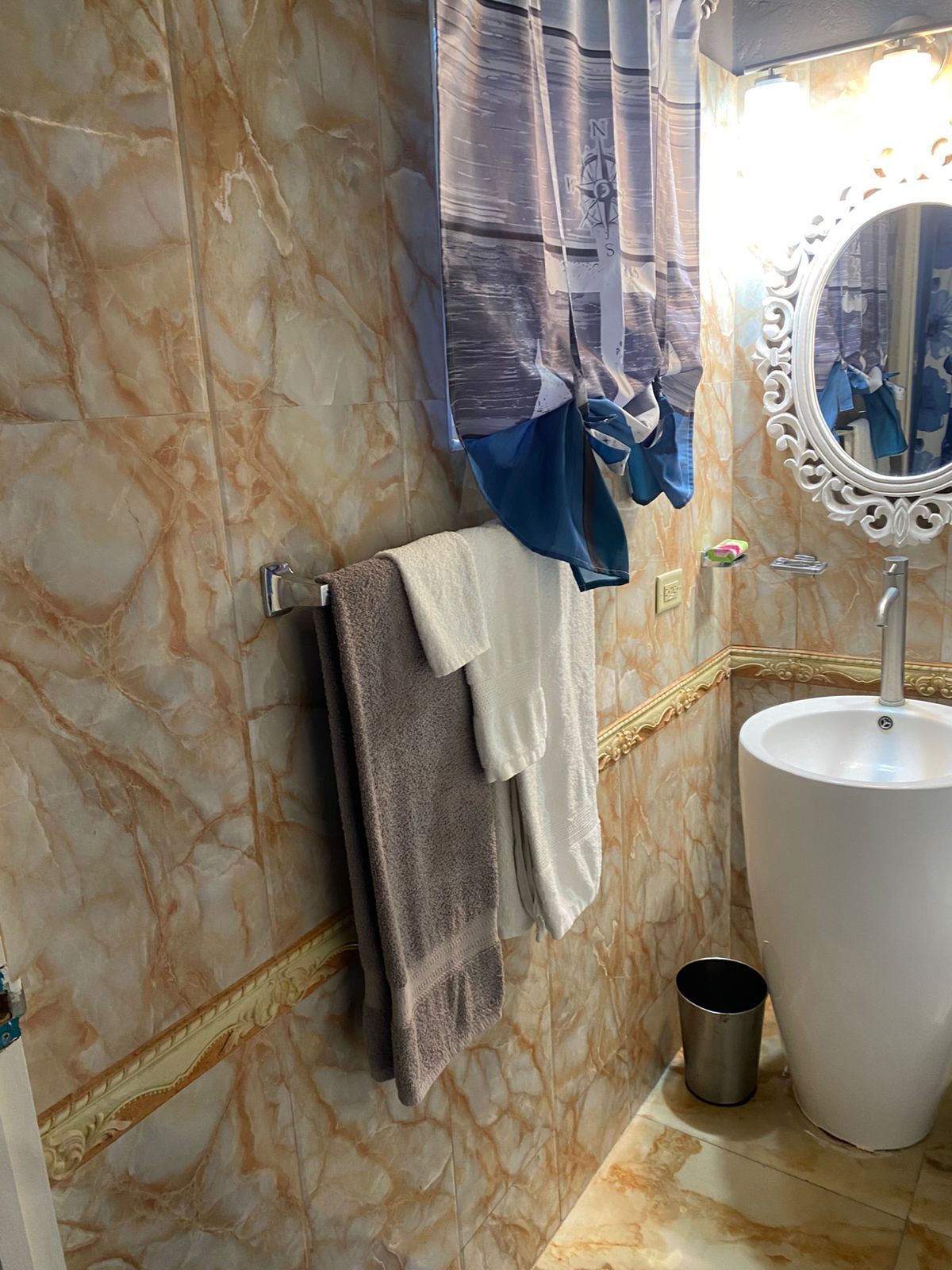 A bathroom with a marble wall, a sink with a mirror, and towels hanging on a rack.