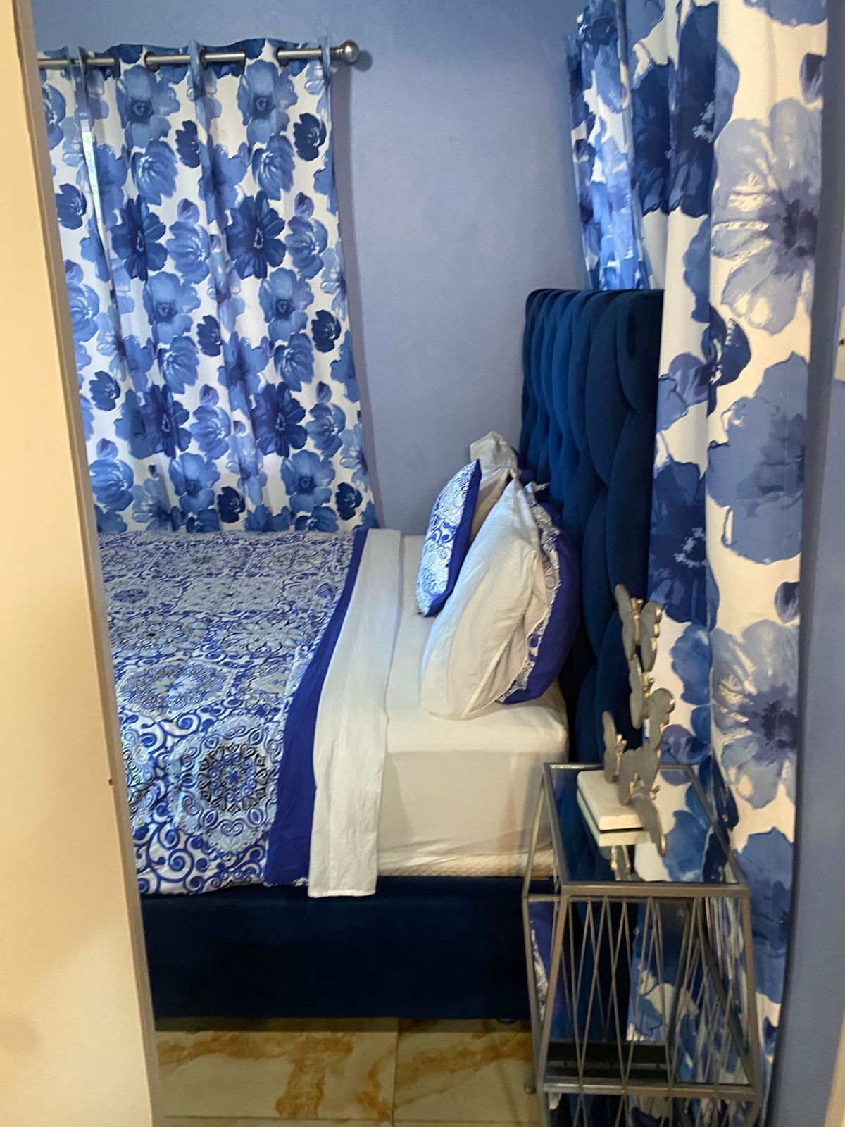 Un dormitorio con cama, mesita de noche y cortinas con estampado floral azul.