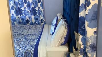 Un dormitorio con cama, mesita de noche y cortinas con estampado floral azul.
