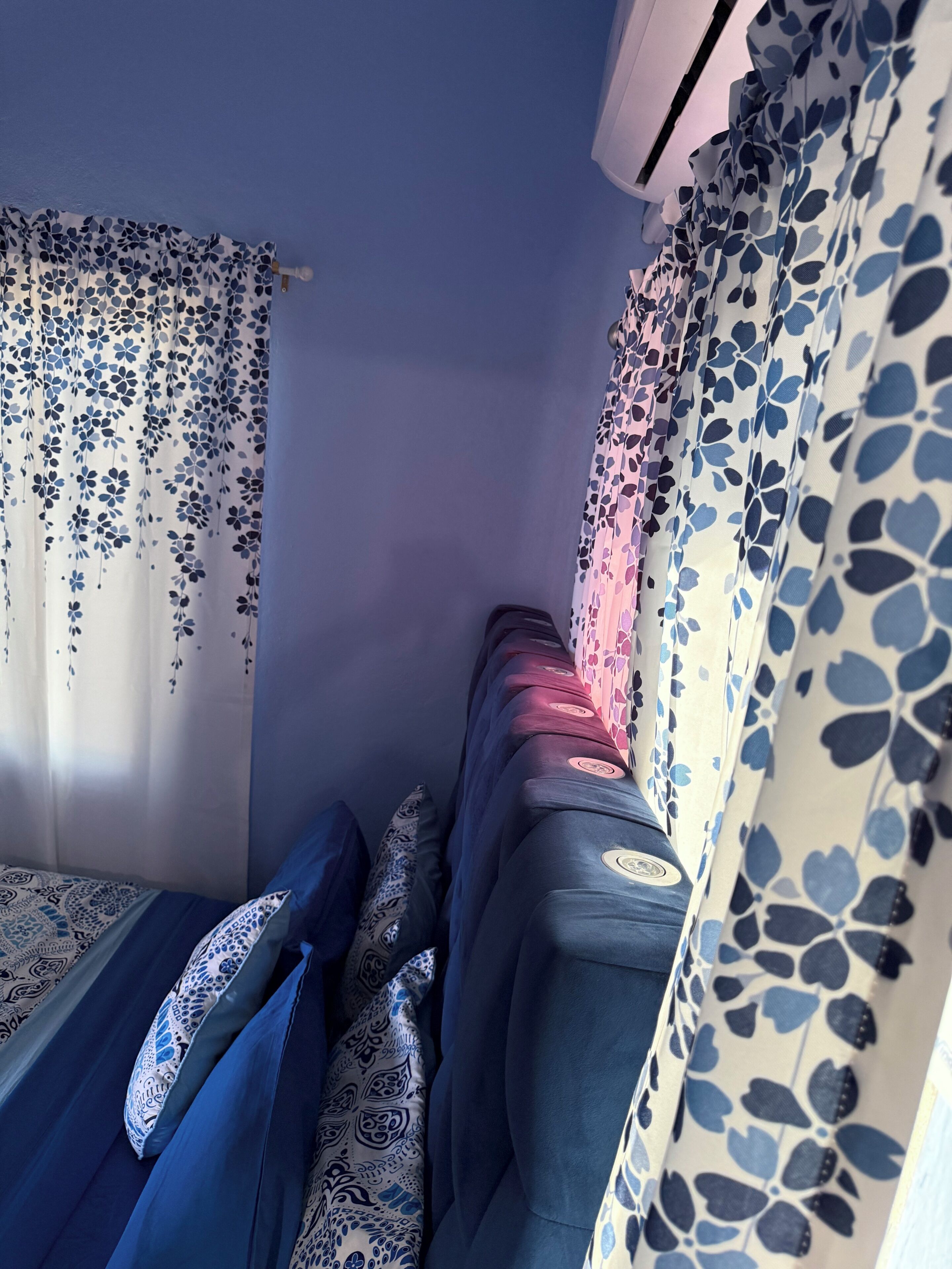 A narrow train compartment with a single bed, patterned curtains, and a window.