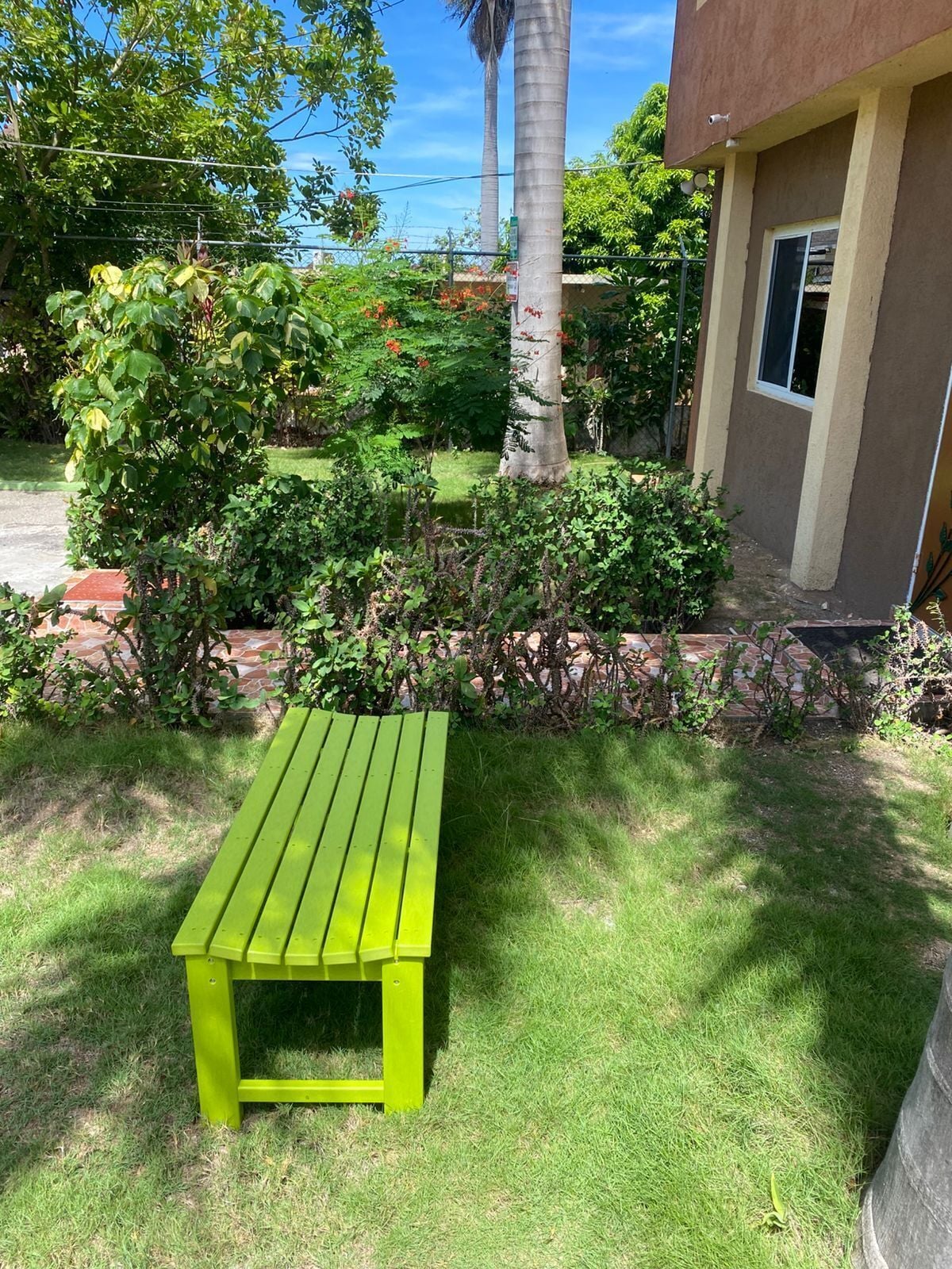 Eine grüne Holzbank in einer Gartenanlage, im Hintergrund ein Gebäude.