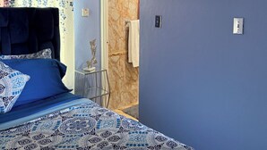 Un dormitorio con cama, un cuadro y un baño visible a través de una puerta abierta.
