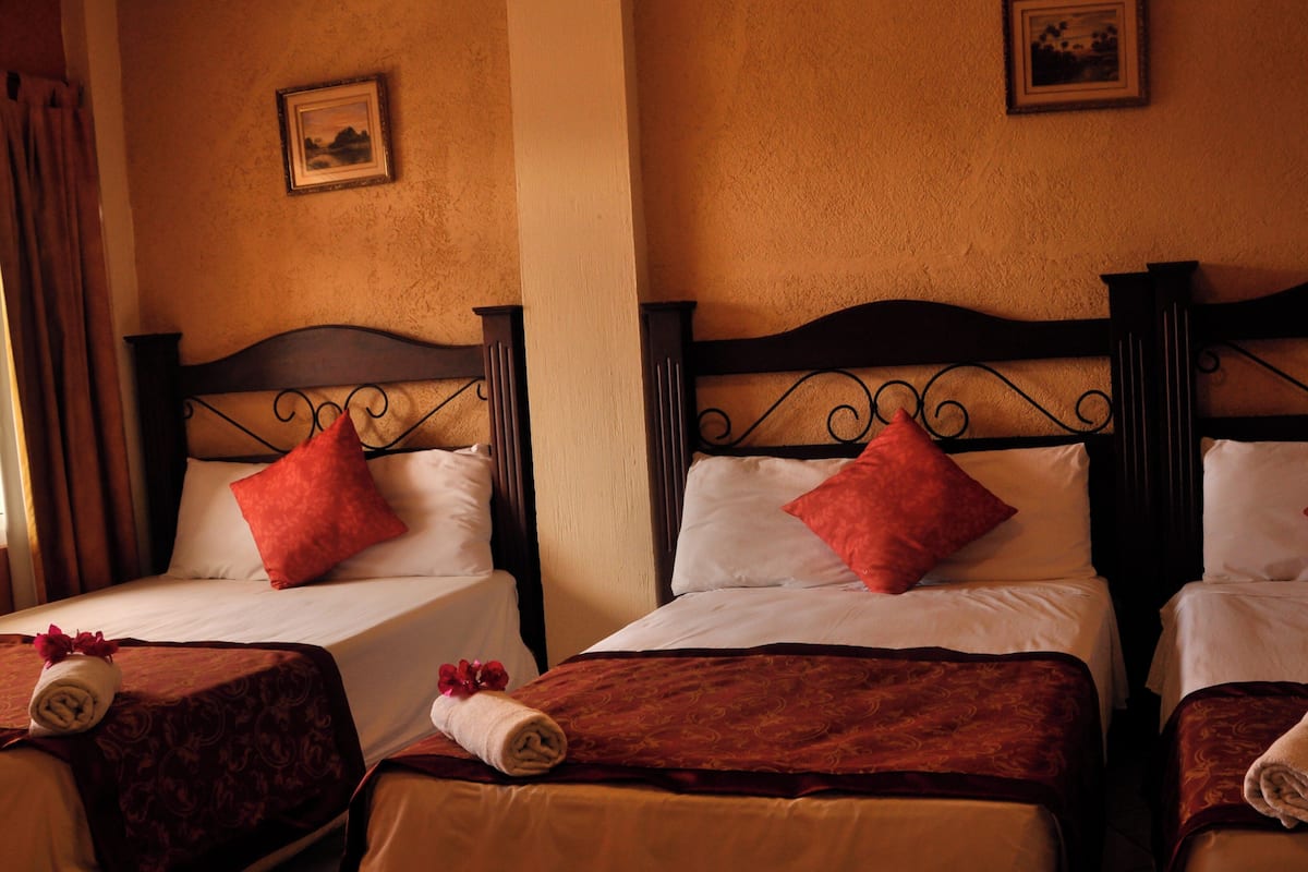 Three double beds with dark wooden headboards, white linens, and red pillows. Each bed has a rolled towel with a red flower.