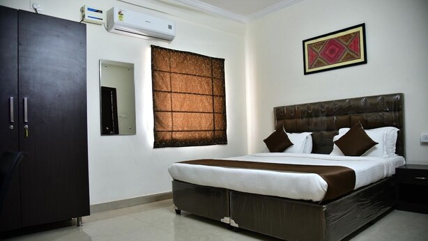 A bedroom with a large bed, a wardrobe, a mirror, an air conditioner, and a decorative wall piece.