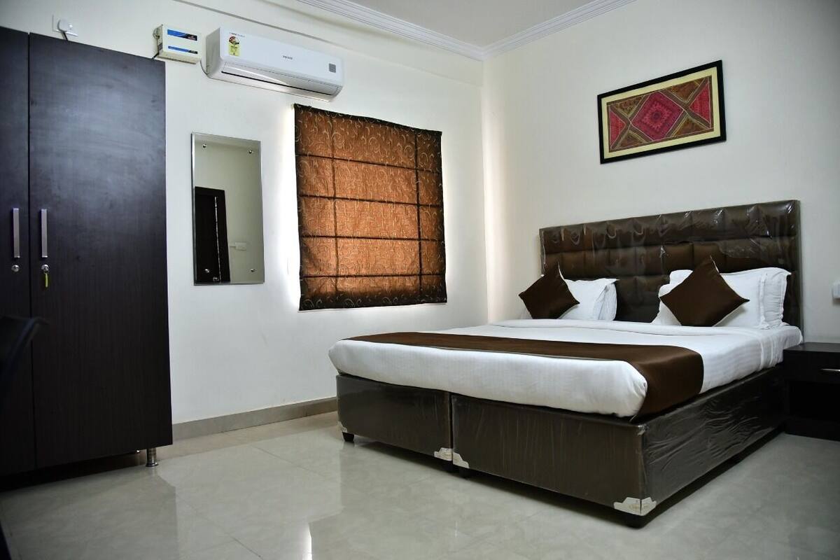 A bedroom with a large bed, a wardrobe, a mirror, an air conditioner, and a decorative wall piece.