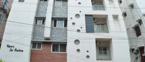 Un edificio residencial de varios pisos con un diseño moderno, que cuenta con una escalera central, balcones y una entrada con portón.