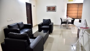 A modern living room with a black leather sofa set, a small black armchair, a dining table with chairs, and a kitchen area with a white appliance.