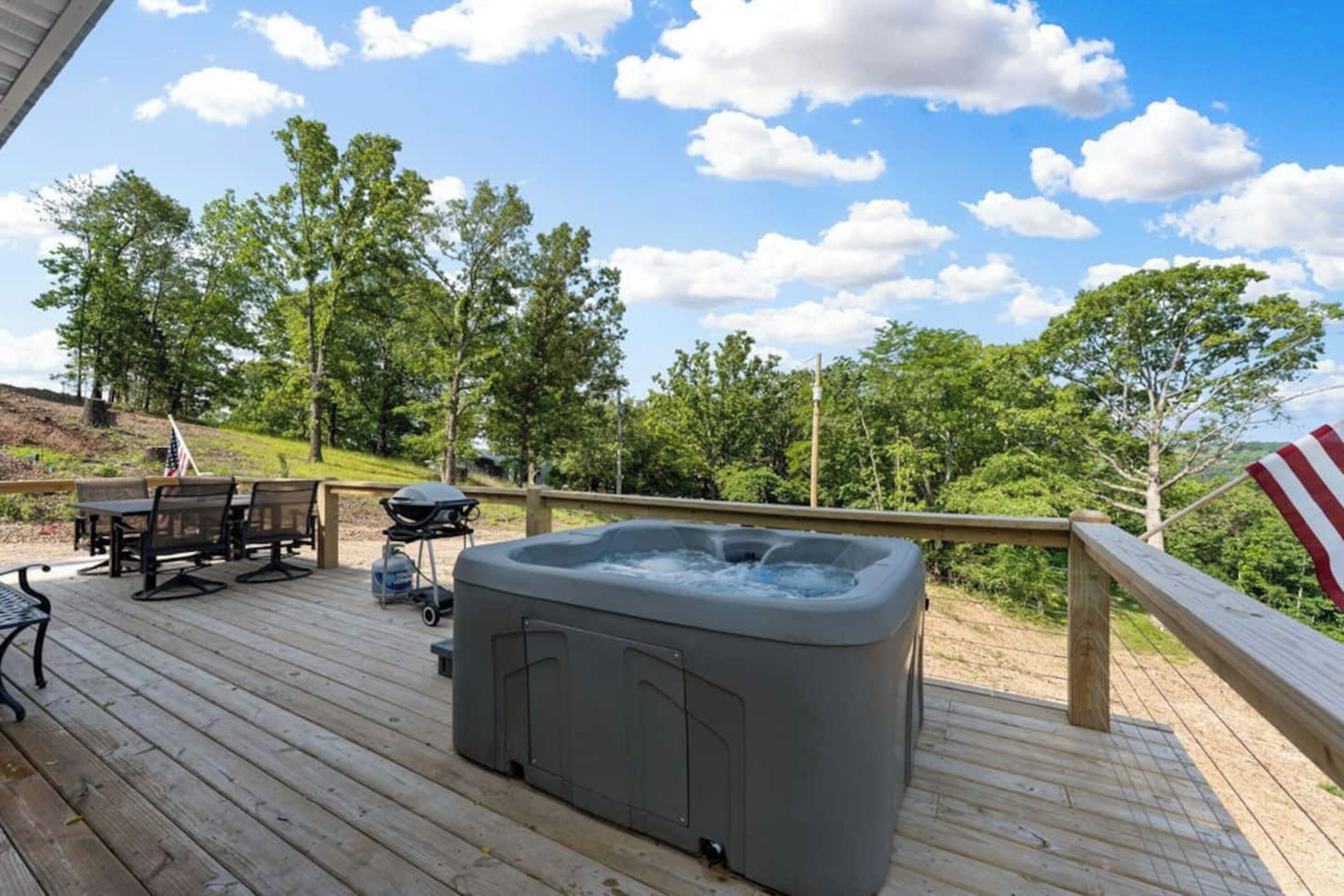 Une terrasse en bois avec un jacuzzi, du mobilier d’extérieur et un drapeau américain.