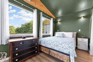 A bedroom with a bed, dresser, nightstand, and windows with curtains. - Romantic Lake Haven - Couples' Cabin (Omaha)