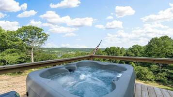 Un bain à remous sur une terrasse en bois, offrant une vue panoramique sur les arbres et les collines.