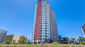 A tall, multi-story hotel with a red and white facade, located near a beach with palm trees and a sandy shoreline.