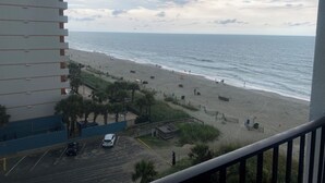 A beach view from a balcony with a parking area and a building with balconies.